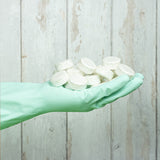 An adult hand wearing a washing glove and holding a bunch of Bio-D dishwasher tablets, showing scale. These dishwasher tablets are available at Babipur.