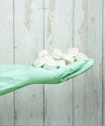 An adult hand wearing a washing glove and holding a bunch of Bio-D dishwasher tablets, showing scale. These dishwasher tablets are available at Babipur.
