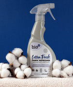A 500ml spray bottle of Bio-D vegan and cruelty free cotton fresh fabric refresher standing on a blanket next to cotton 