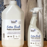 A 5L bottle of Bio-D vegan and cruelty free cotton fresh fabric refresher liquid standing next to a 500ml spray bottle on a wooden surface 