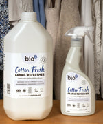 A 5L bottle of Bio-D vegan and cruelty free cotton fresh fabric refresher liquid standing next to a 500ml spray bottle on a wooden surface 
