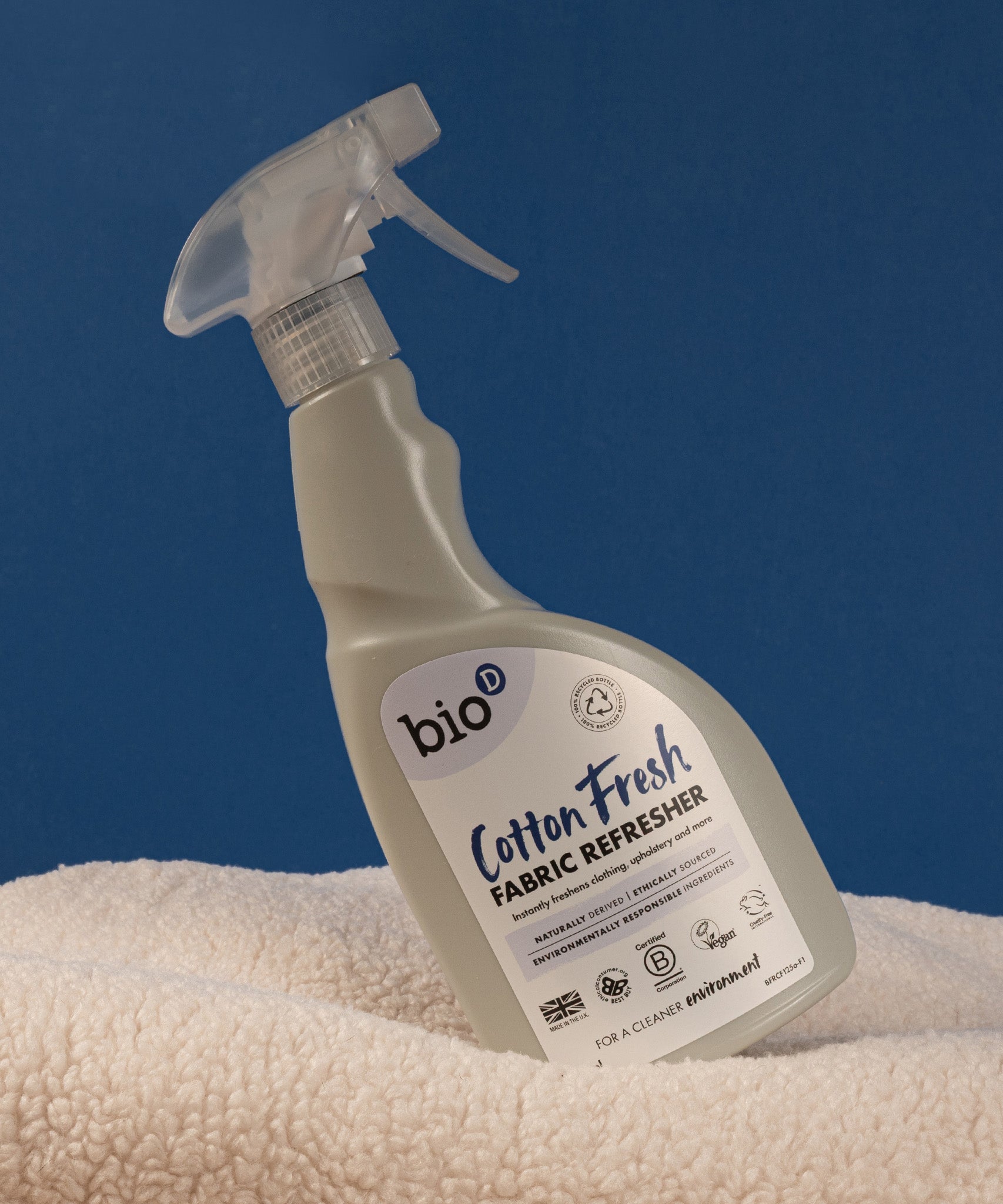 A 500ml spray bottle of Bio-D vegan and cruelty free cotton fresh fabric refresher balancing on a blanket 