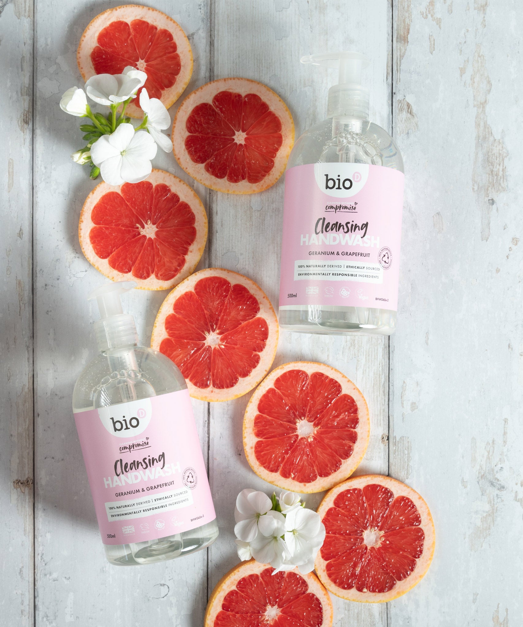 A flatlay image of 2 bottles of 500ml Bio-D cleansing hand wash  in geranium and grapefruit lined up next to slices of grapefruit. This hand wash is available at Babipur.