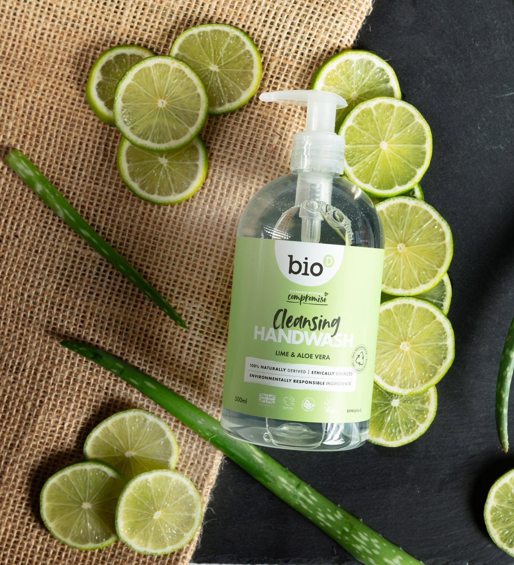 A flatlay image of a 500ml bottle of Bio-D cleansing hand wash  in lime and aloe vera lined up next to slices of lime and aloe. This hand wash is available at Babipur.