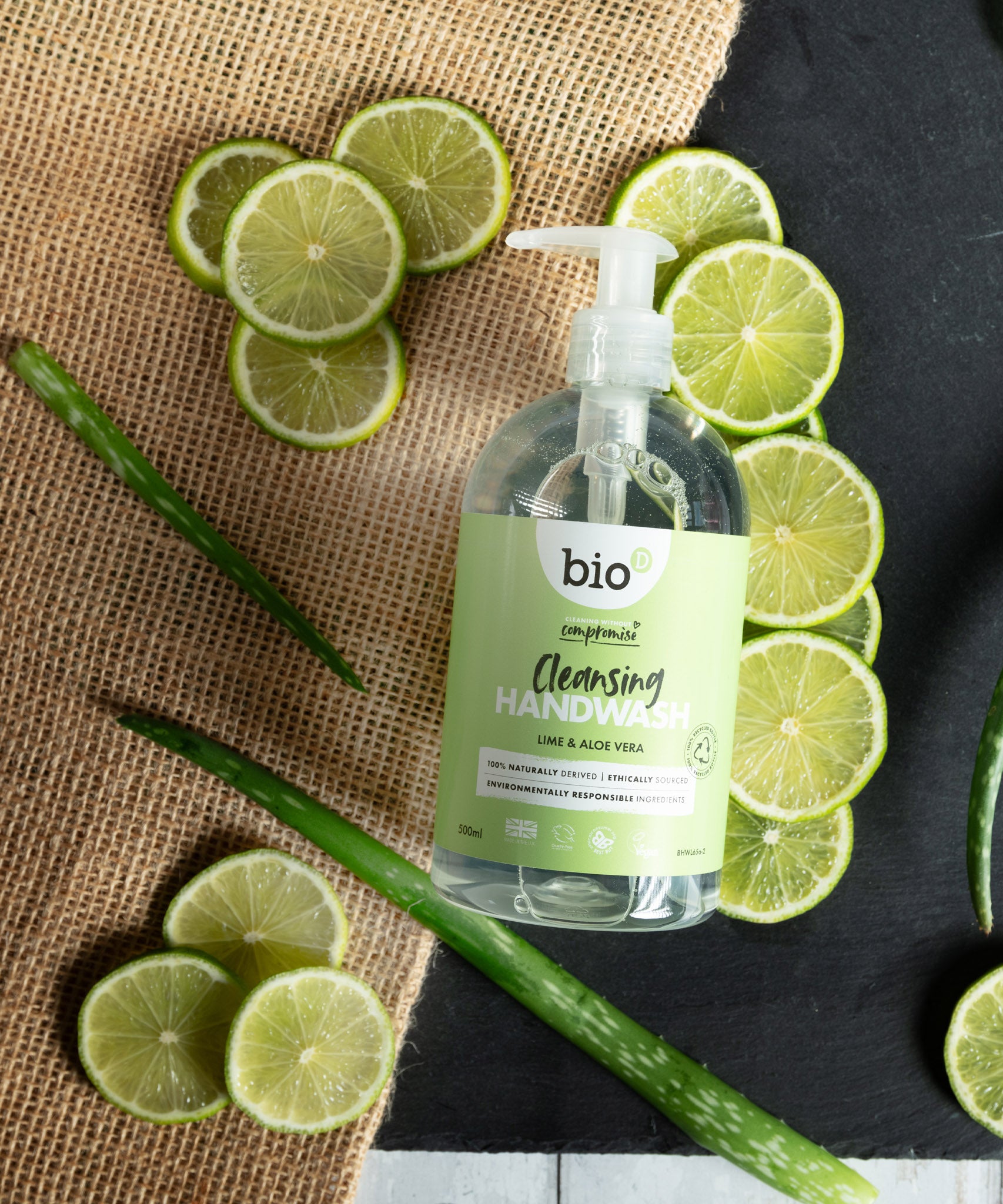 A flatlay image of a 500ml bottle of Bio-D cleansing hand wash  in lime and aloe vera lined up next to slices of lime and aloe. This hand wash is available at Babipur.
