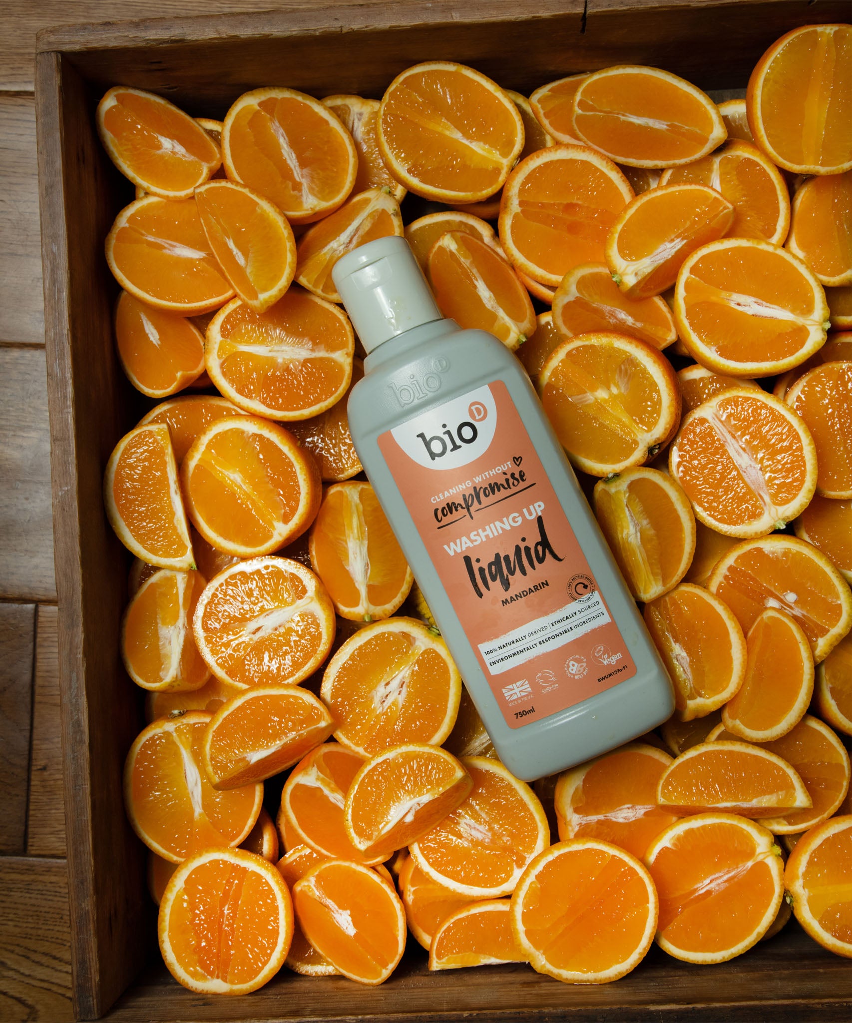 A Bio-D 750ml mandarin washing up liquid bottle in a crate of sliced mandarins. This washing up liquid is available at Babipur 
