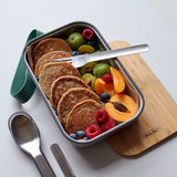 A close up of the Black + Blum stainless steel cutlery set next to a olive original Lunchbox with food inside