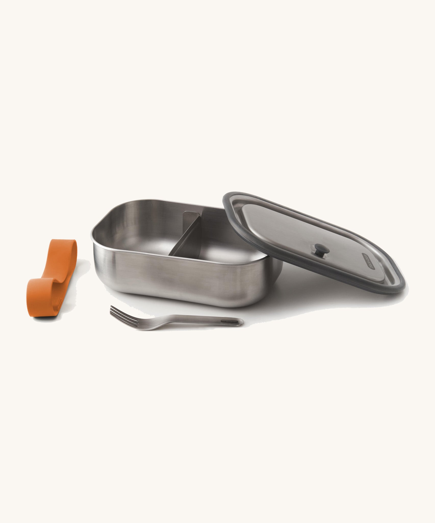 Black+Blum Large Leak Proof Stainless Steel Lunch Box with orange coloured strap. The lid is shown resting on the side of the lunchbox with the strap and fork besides it. This lunchbox is part of a wide range of stainless steel lunch box options available here at Babipur. 