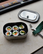A close up of the Black + Blum leakproof stainless steel lunchbox with a olive silicone showing the size of the box with food inside