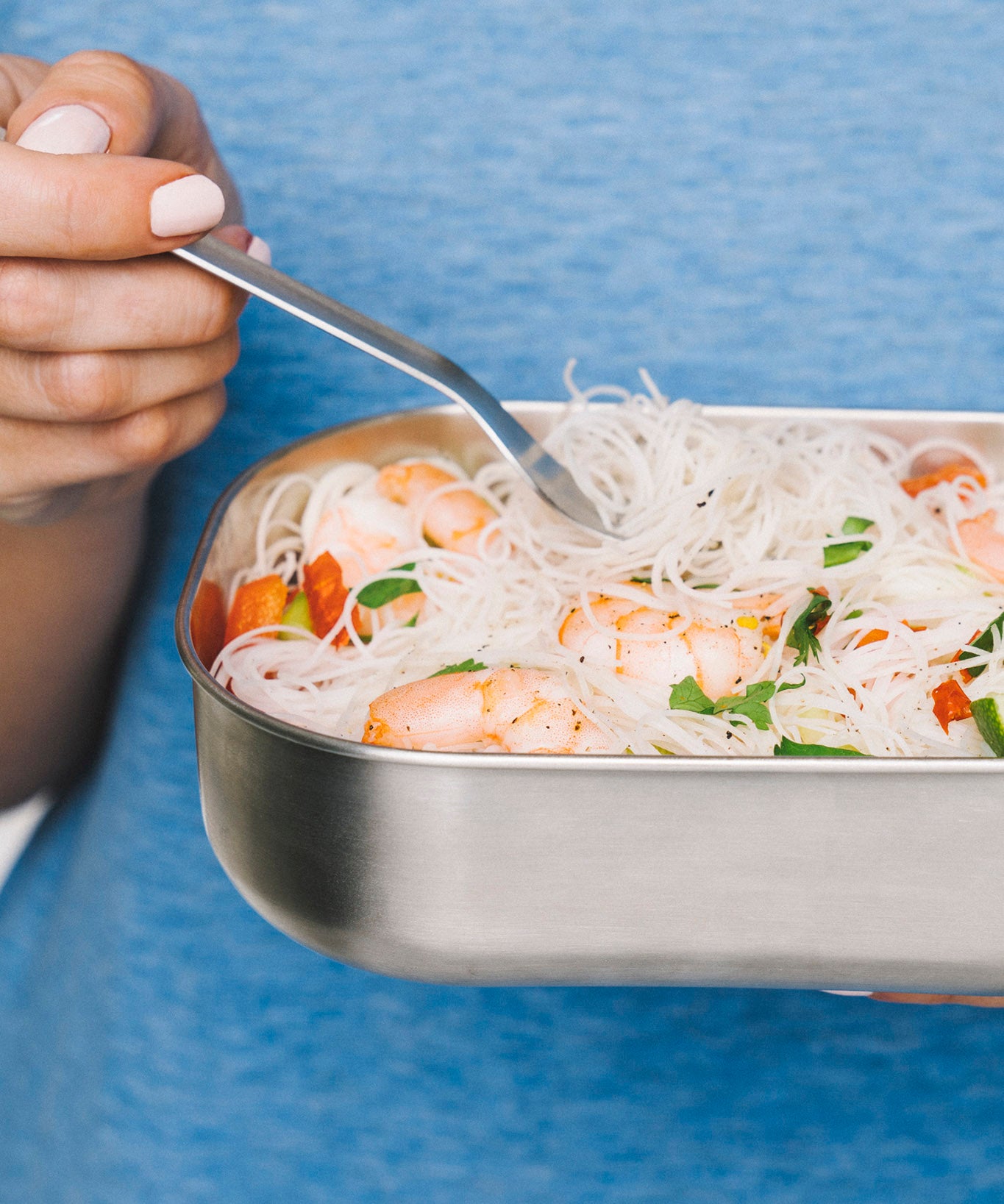 A close up and adult holding the fork from the Black + Blum stainless steel cutlery set and eating from a stainless steel lunchbox
