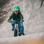 Child riding a bicycle on a gravel path wearing a green helmet