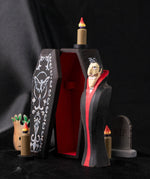 Bumbu handmade and hand painted wooden black coffin in a spooky place scene including a Dracula figure, candles a small gravestone and a small tree.