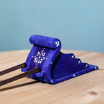 The blue Bumbu Wooden Snow Sleigh Toy is stood on a wooden table with the dark brown wooden reins attached to the front, which are slightly showing in the image