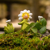 Bumb wooden daisy flower child figure with hand painted facial features standing on moss next to a white flowers