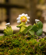 Bumb wooden daisy flower child figure with hand painted facial features standing on moss next to a white flowers
