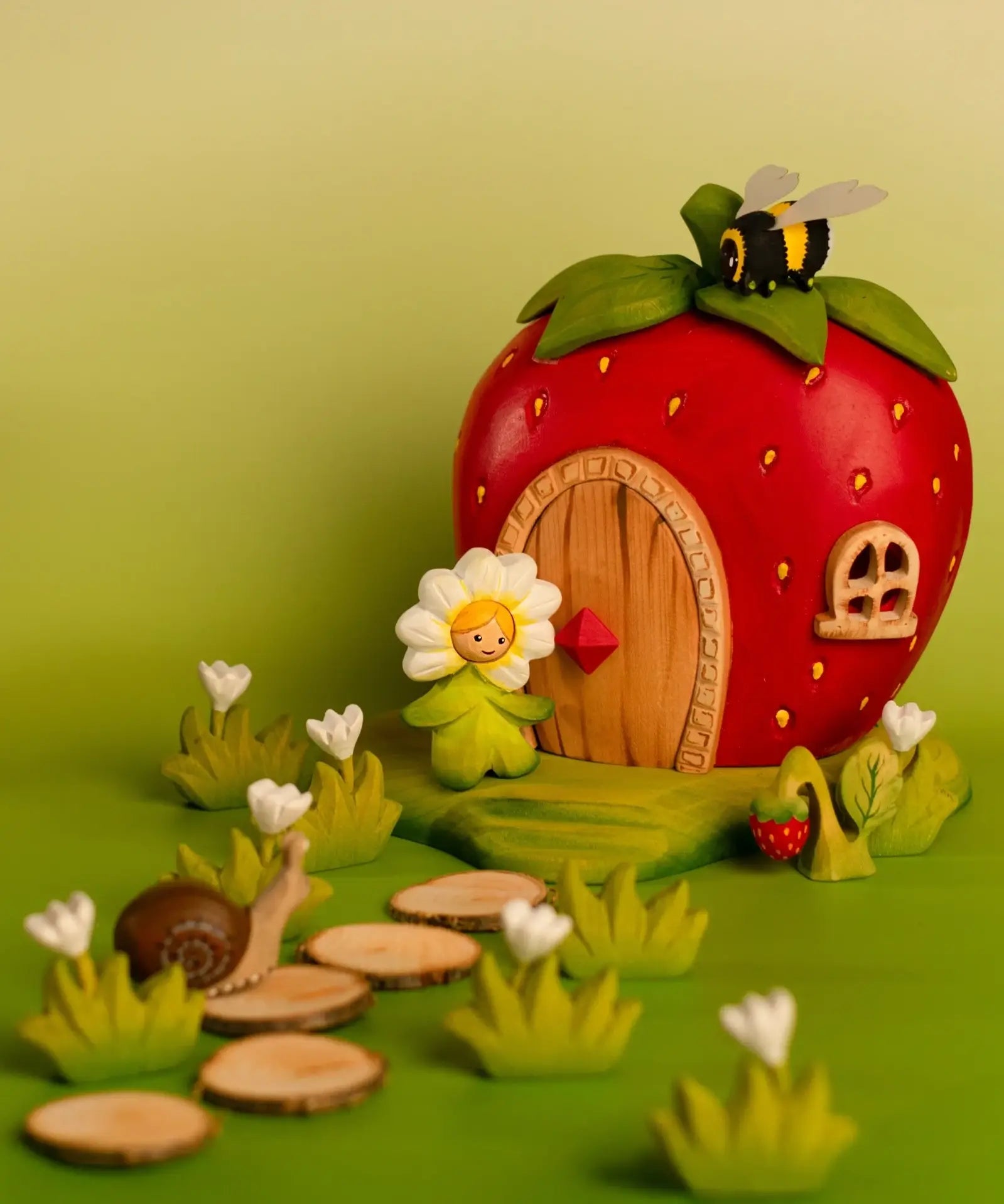 Bumbu wooden daisy flower child figure standing next to a wooden strawberry house with a bee on top and snail