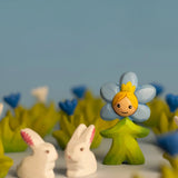 Bumbu wooden daisy flower child figure with hand painted facial features standing next to white rabbit figures