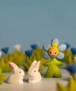 Bumbu wooden daisy flower child figure with hand painted facial features standing next to white rabbit figures