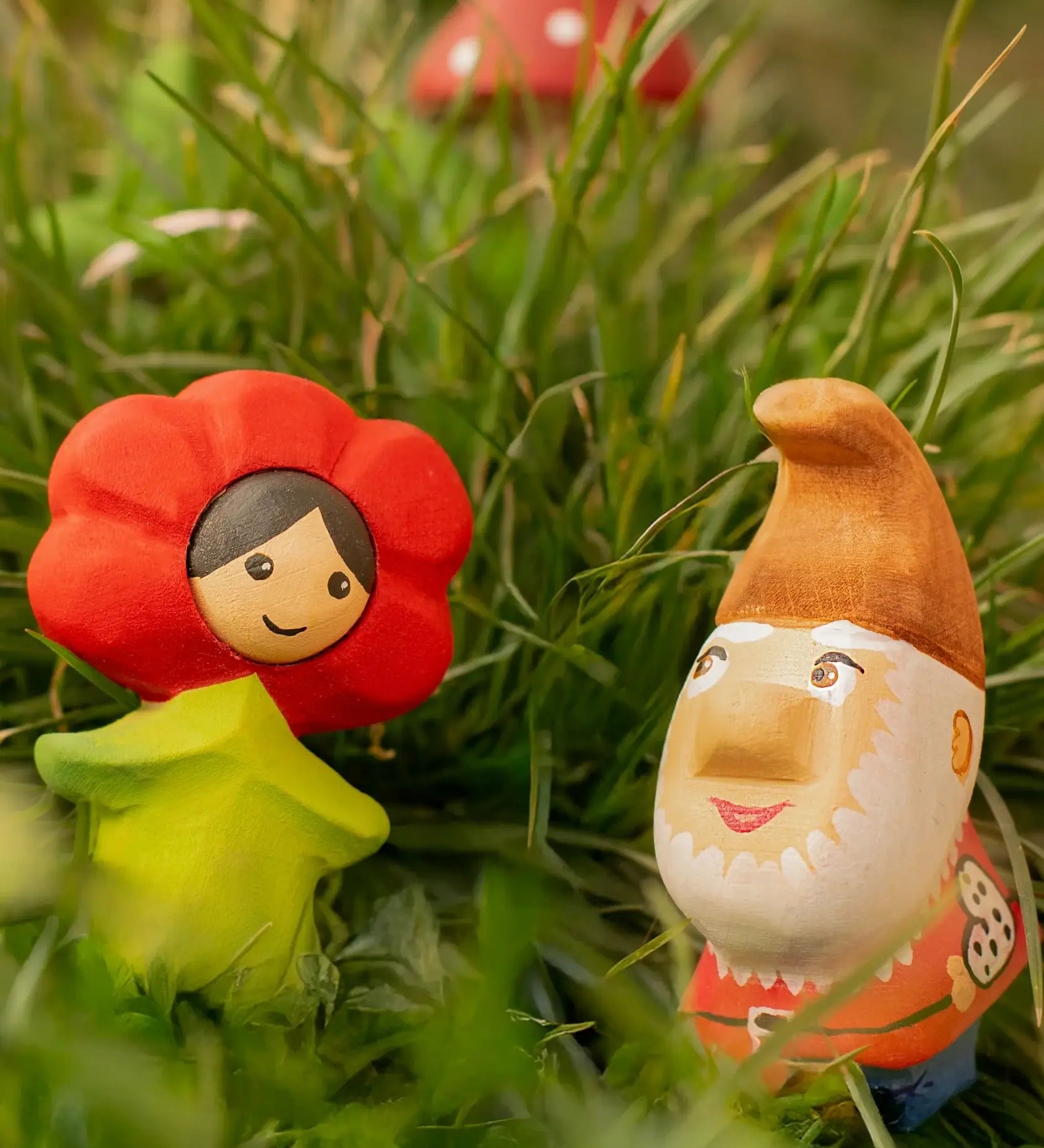 Bumbu wooden red poppy flower child figure next to a wooden gnome figure standing in grass
