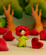 Bumbu wooden red poppy flower child figure in a playscene with red wooden hearts and trees in the background