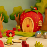 Bumbu wooden poppy flower child figure standing next to a wooden strawberry house and trees in the background