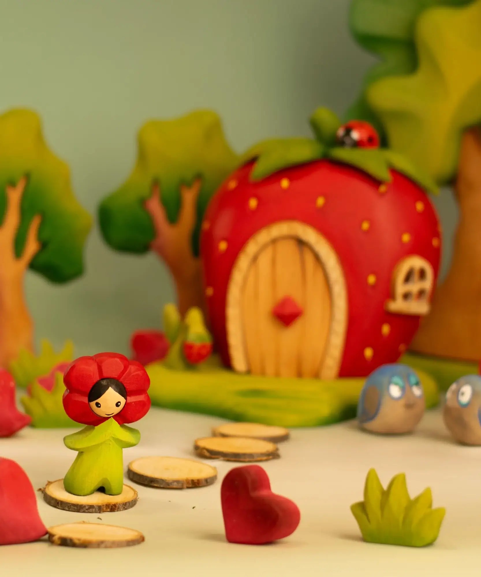 Bumbu wooden poppy flower child figure standing next to a wooden strawberry house and trees in the background
