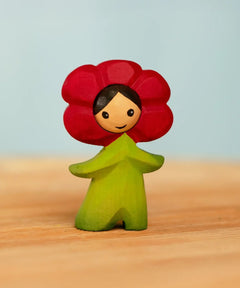 Bumbu handcrafted wooden red poppy flower child figure with hand painted facial features standing on a wooden surface