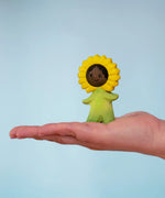 Bumbu wooden sunflower figure with hand painted facial features standing on a adult hand