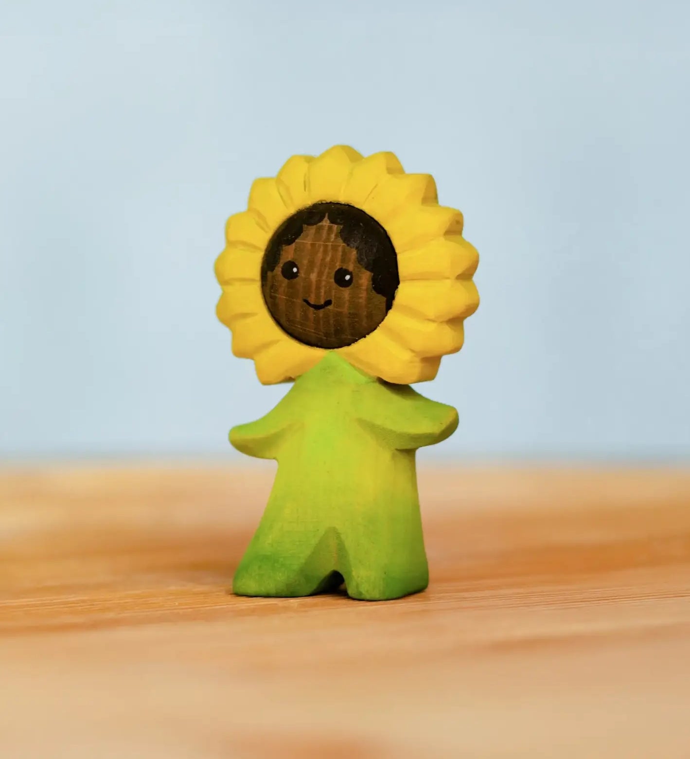 Bumbu handcrafted wooden sunflower figure with hand painted facial features standing on a wooden surface