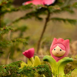 Bumbu wooden pink tulip figure showing hand painted facial features standing in moss with a butterfly in the background.