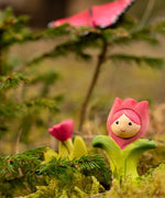 Bumbu wooden pink tulip figure showing hand painted facial features standing in moss with a butterfly in the background.