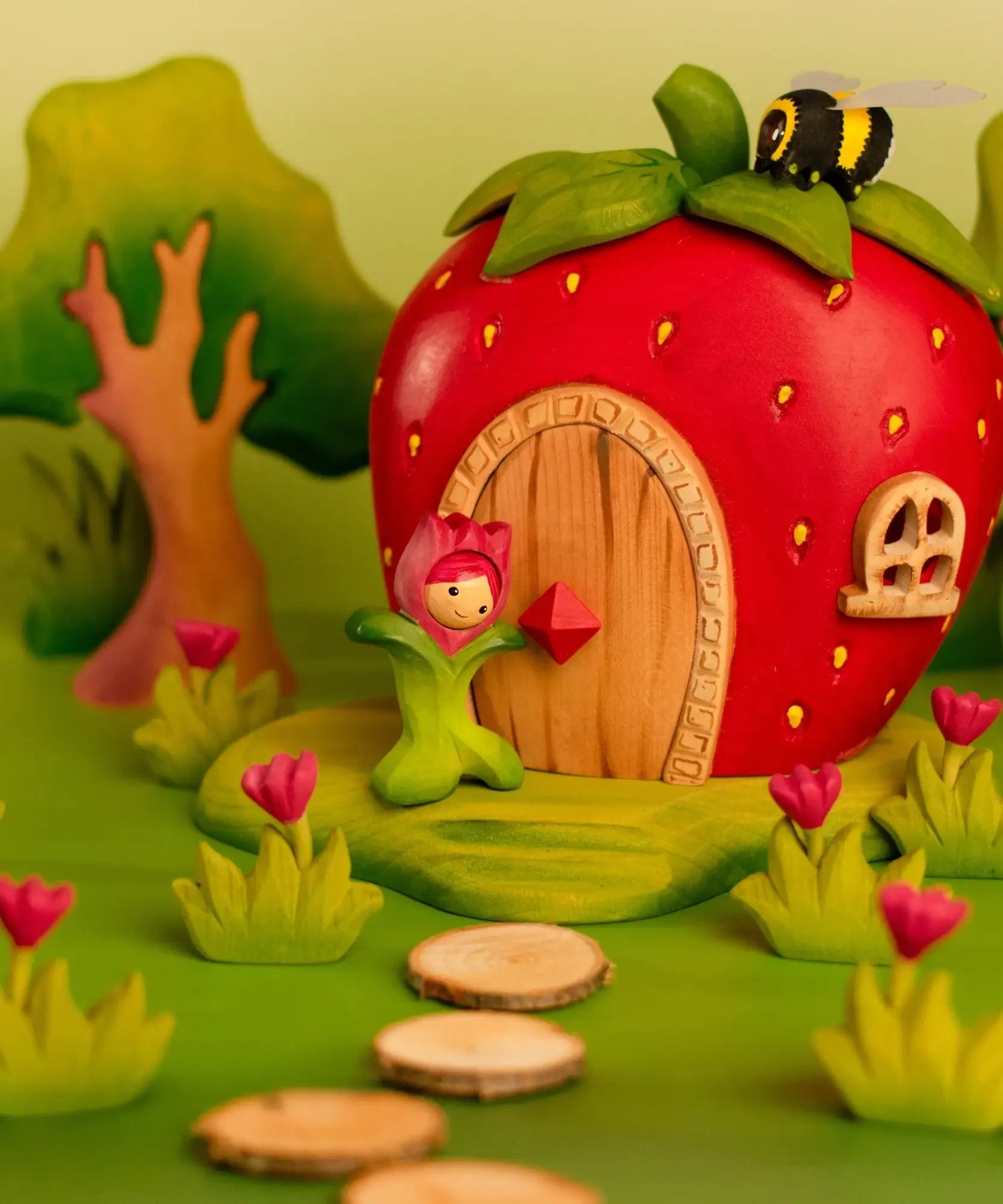 Bumbu wooden pink tulip figure standing next to a wooden strawberry house with a bee on top