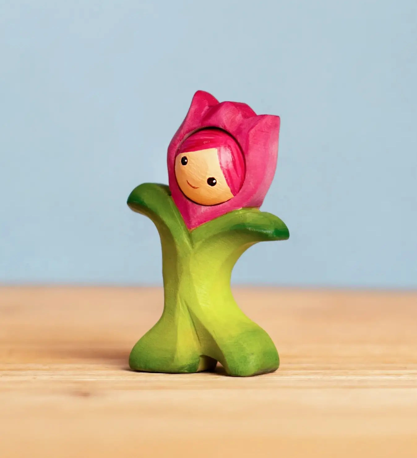 Bumbu handcrafted wooden pink tulip figure showing hand painted facial features standing on a wooden surface 