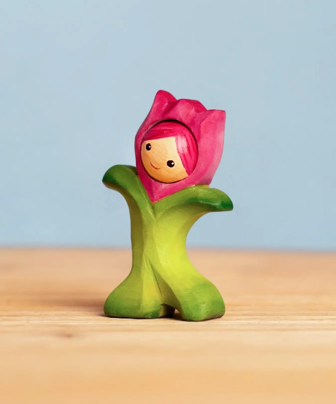 Bumbu handcrafted wooden pink tulip figure showing hand painted facial features standing on a wooden surface 