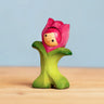 Bumbu handcrafted wooden pink tulip figure showing hand painted facial features standing on a wooden surface 
