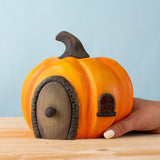 An adult hand holding the Bumbu handmade and hand painted wooden halloween orange pumpkin house showing scale