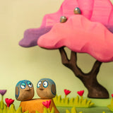 Bumbu hand crafted wooden love birds figure set in a playscene with a pink  tree in the background.