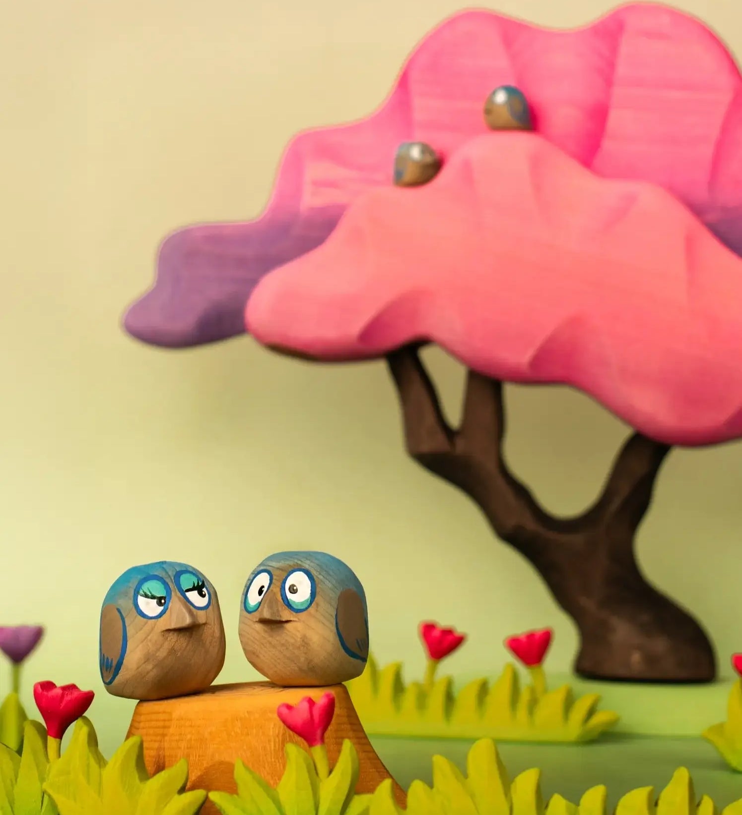 Bumbu hand crafted wooden love birds figure set in a playscene with a pink  tree in the background.