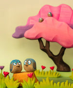 Bumbu hand crafted wooden love birds figure set in a playscene with a pink  tree in the background.