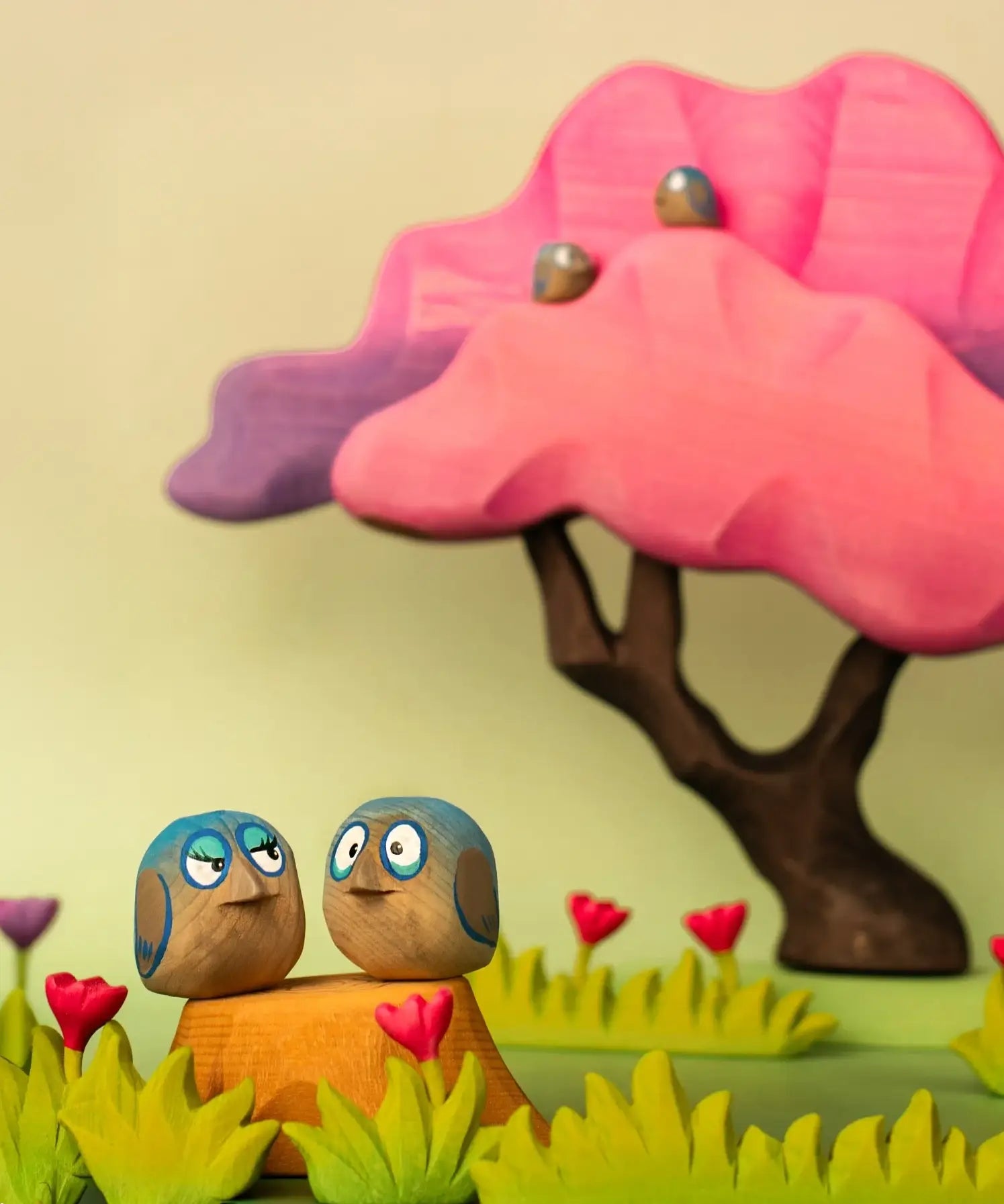 Bumbu hand crafted wooden love birds figure set in a playscene with a pink  tree in the background.