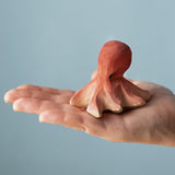 An adult hand holding the Bumbu handmade and hand painted wooden octopus figure showing size