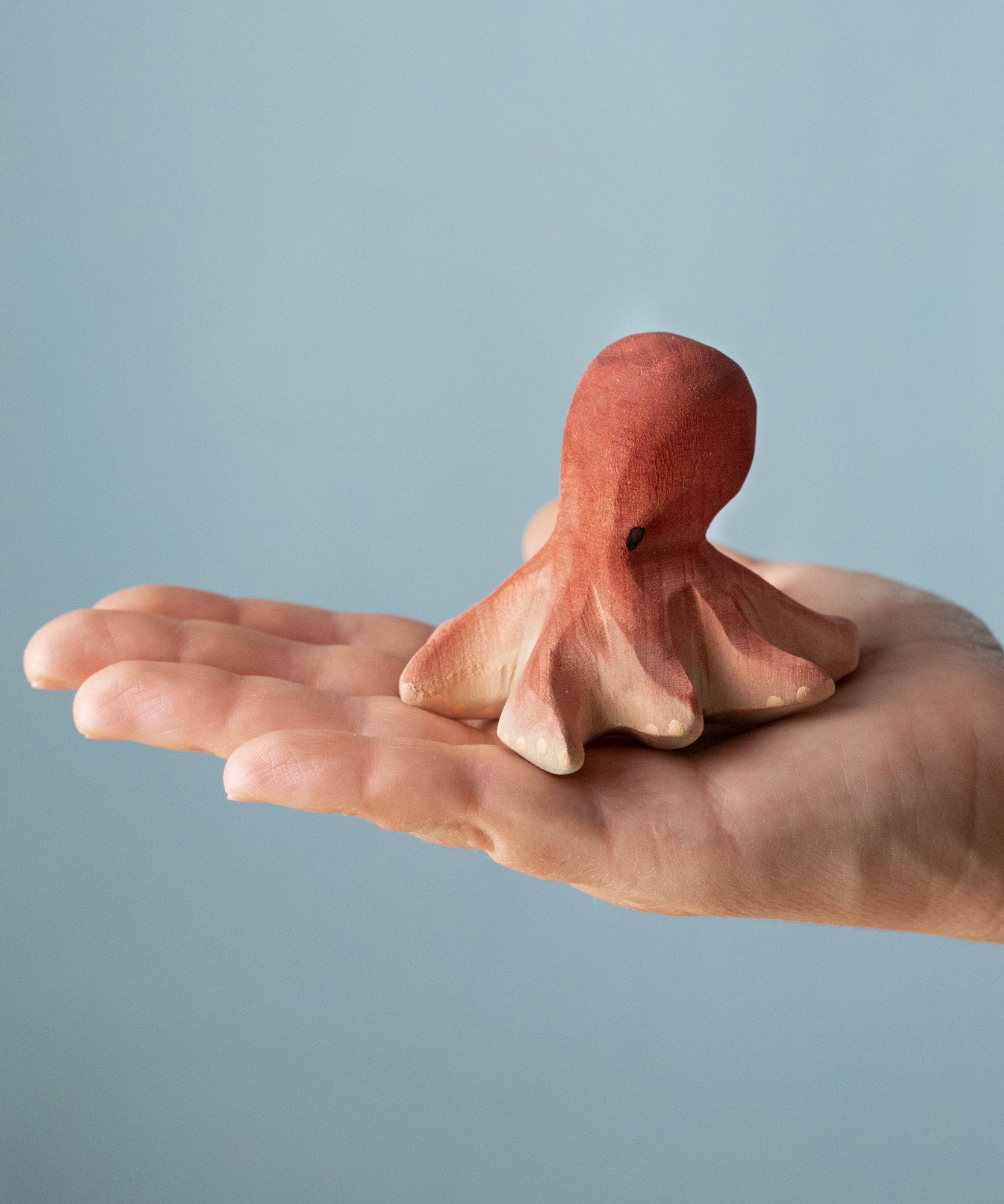 An adult hand holding the Bumbu handmade and hand painted wooden octopus figure showing size
