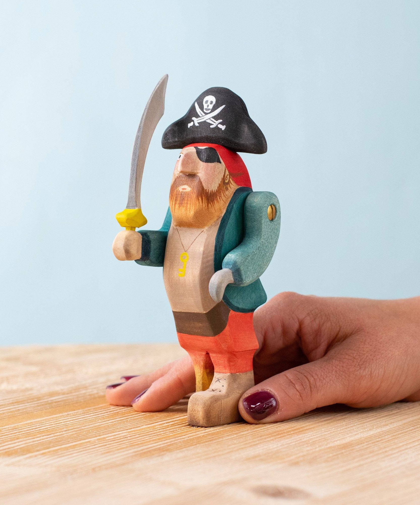 An adult hand holding the Bumbu handmade and hand painted pirate wooden figure showing size