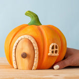An adult hand holding the Bumbu handmade and hand painted wooden orange pumpkin house showing scale