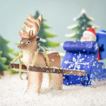 A snowy scene of a Bumbu Reindeer pulling the Bumbu Santa in the Blue Snow Sleigh. In the background are snowy green Bumbu Trees