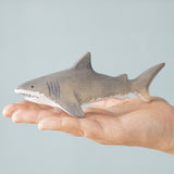 An adult hand holding the Bumbu handmade and hand painted wooden grey shark figure showing size