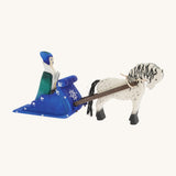 A side view of the Bumbu Snow Queen with a white and black Bumbu Horse attached by the rein to the blue Bumbu Snow Sleigh. The queen is sat in the back of the sleigh