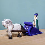 The Snow Queen with a white and black Bumbu Horse attached by the rein to the blue Bumbu Snow Sleigh. The queen is sat in the back of the sleigh