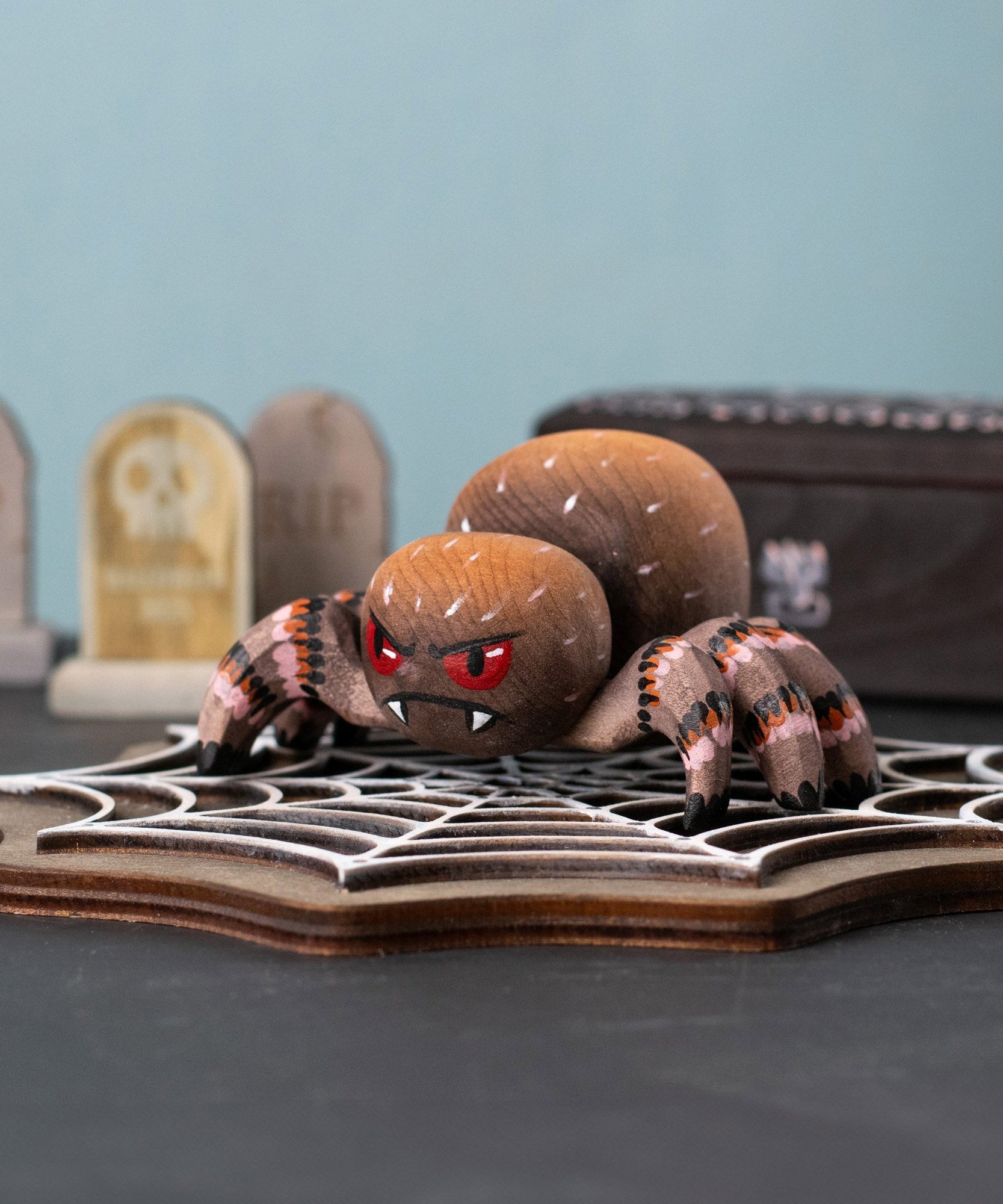 Bumbu handmade and hand painted wooden spider figure with hand painted facial features resting on a wooden Bumbu cobweb in a spooky play scene