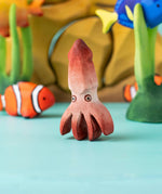 Bumbu handmade and hand painted wooden squid figure with cute painted on eyes with other Bumbu ocean themed figures in the background 